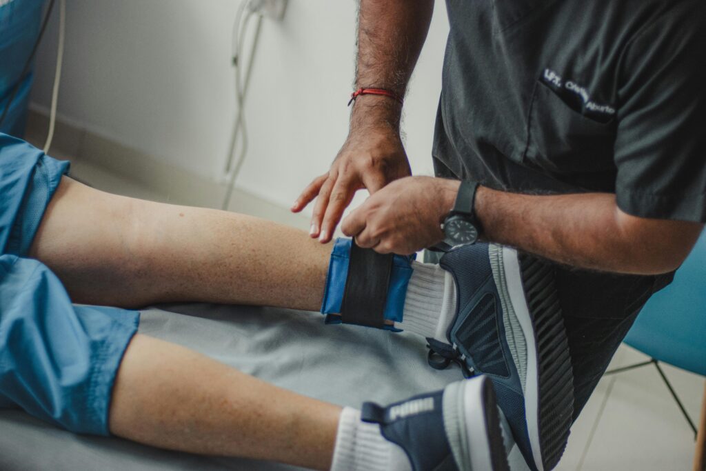 A physiotherapist adjusts a leg strap on a patient in a clinical setting.